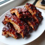 Zbliżenie na porcję soczystych żeberka pieczone w sosie BBQ, obficie polane błyszczącym, ciemnym sosem.