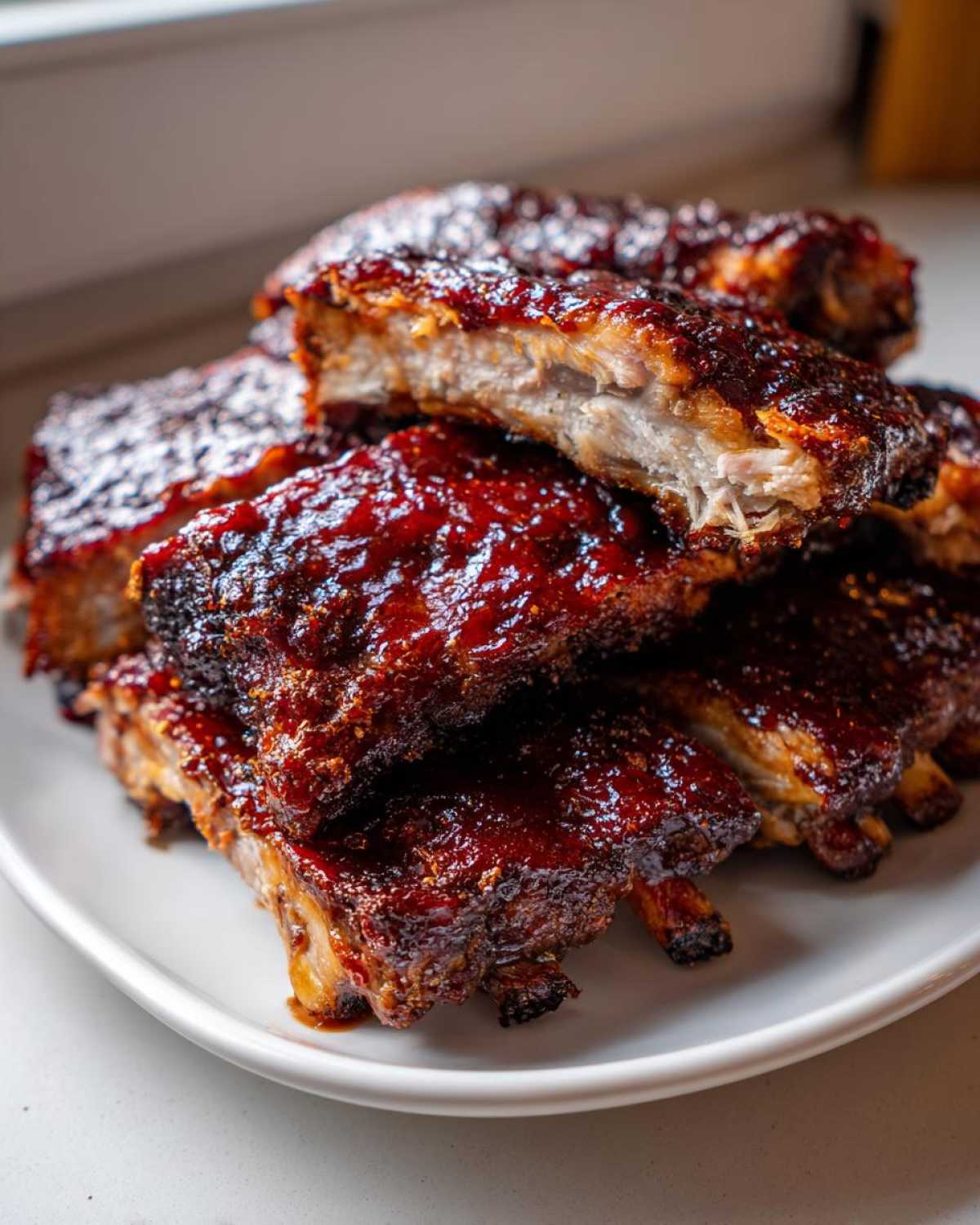 Zbliżenie na stos soczystych, miękkich żeberka pieczone w sosie BBQ, z widocznym przekrojem mięsa.