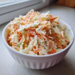 Zbliżenie na kremową Sałatka coleslaw z młodej kapusty z tartą marchewką w białej miseczce.