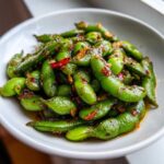 Zbliżenie na miskę pełną Bób smażony z chili i czosnkiem, polany sosem.