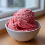 Zbliżenie na dwie gałki różowych Domowe lody truskawkowe z 3 składników w białej miseczce.