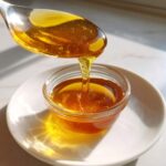 Gęsty, bursztynowy syrop z mniszka lekarskiego spływający z metalowej łyżki do małej szklanej miseczki.