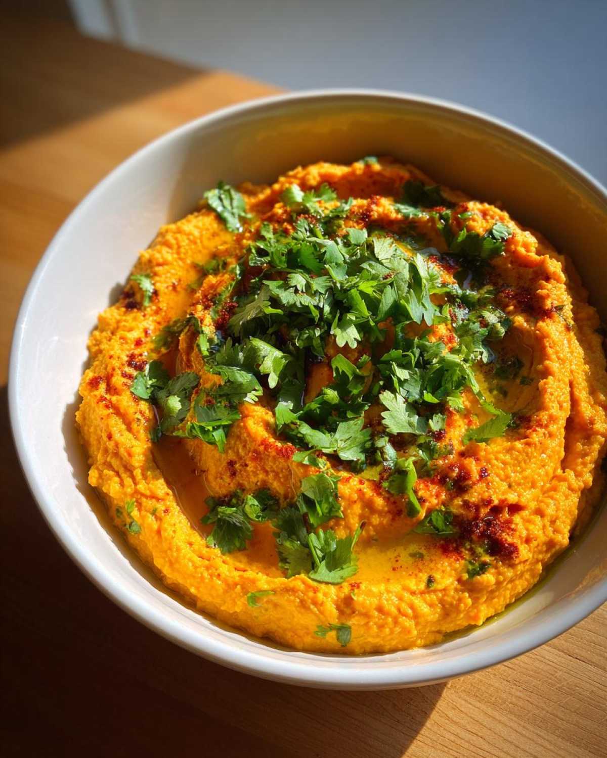 Kremowy, pomarańczowy hummus z pieczoną marchwią i kolendrą, polany oliwą.