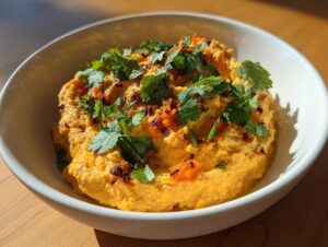 Kremowy hummus z pieczoną marchwią i kolendrą podany w białej misce.