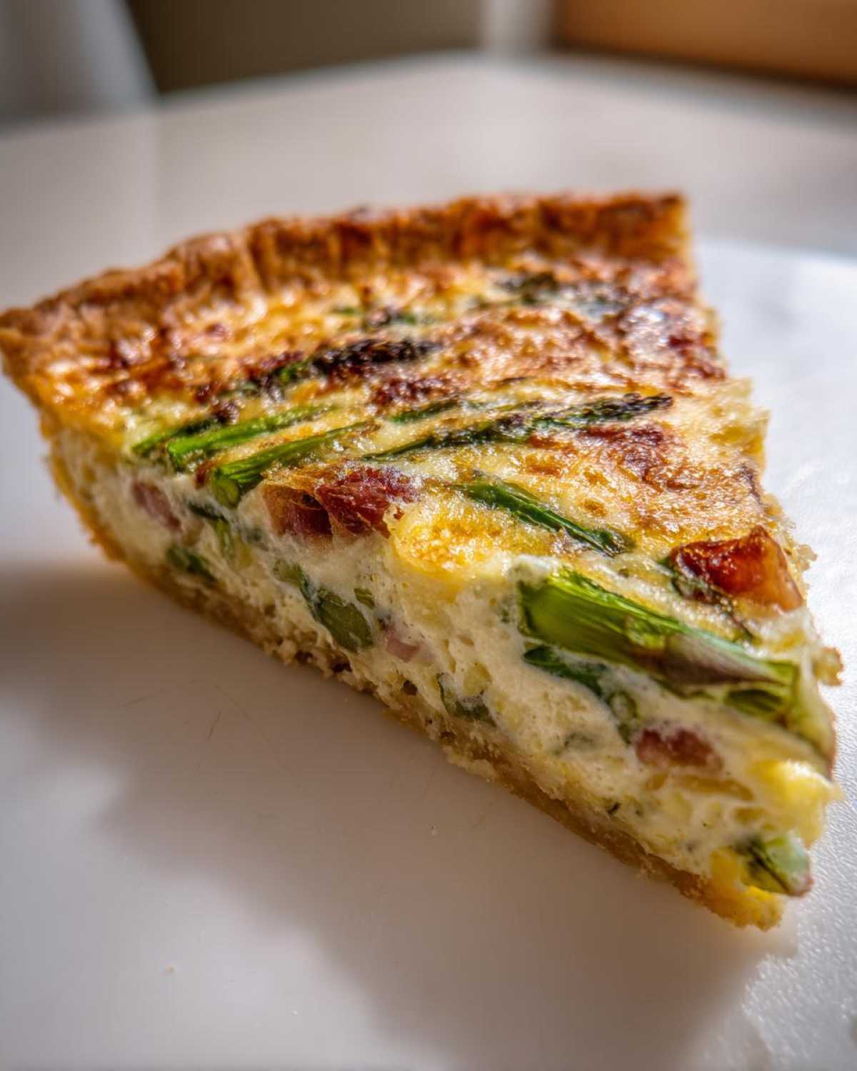 Zbliżenie na kawałek Quiche ze szparagami i boczkiem, widoczny złocisty spód i kremowe nadzienie.