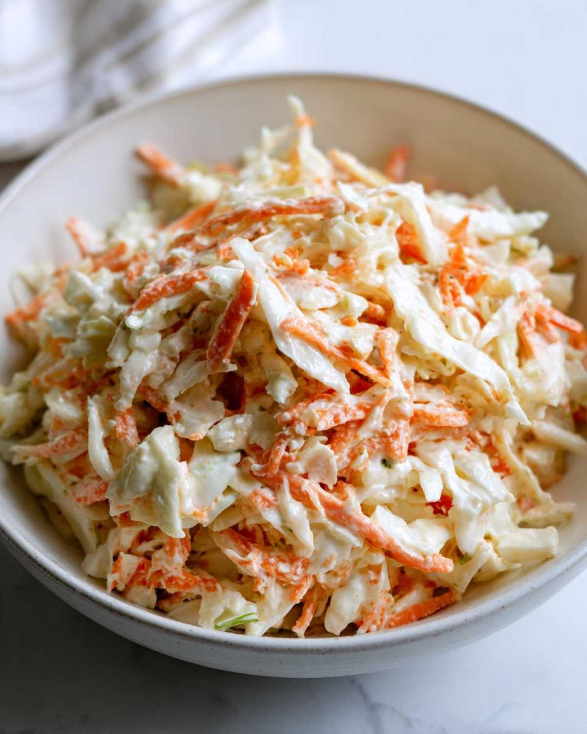 Zbliżenie na miskę pełną kremowej sałatki coleslaw z młodej kapusty i startej marchewki.