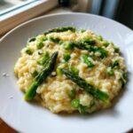 Kremowe Risotto ze szparagami i parmezanem podane na białym talerzu, z widocznymi kawałkami zielonych szparagów.
