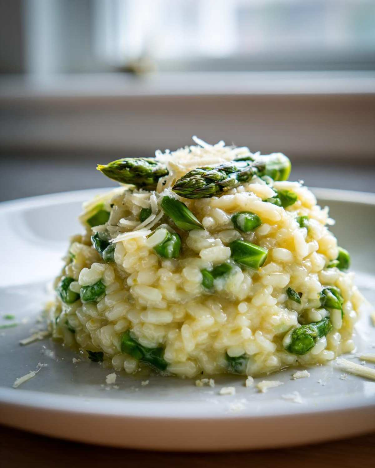 Porcja kremowego Risotto ze szparagami i parmezanem, udekorowana wierzchołkami szparagów.