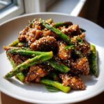 Zbliżenie na Kurczak Teriyaki ze szparagami i sezamem, polany sosem w białym talerzu.