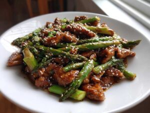 Zbliżenie na porcję Kurczak Teriyaki ze szparagami i sezamem, polane sosem.