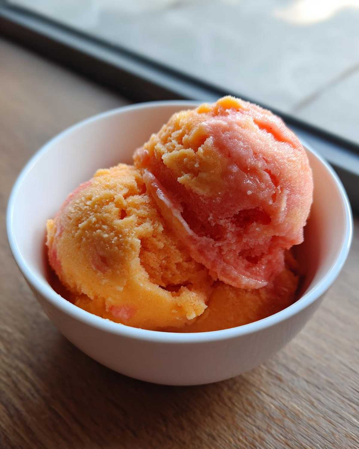 Dwie gałki sorbetu, mango i truskawka, w białej miseczce. Idealne lody mango i truskawka.