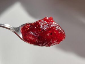 Zbliżenie na łyżkę wypełnioną gęstym, błyszczącym Dżemem truskawkowym z czarnym bzem.