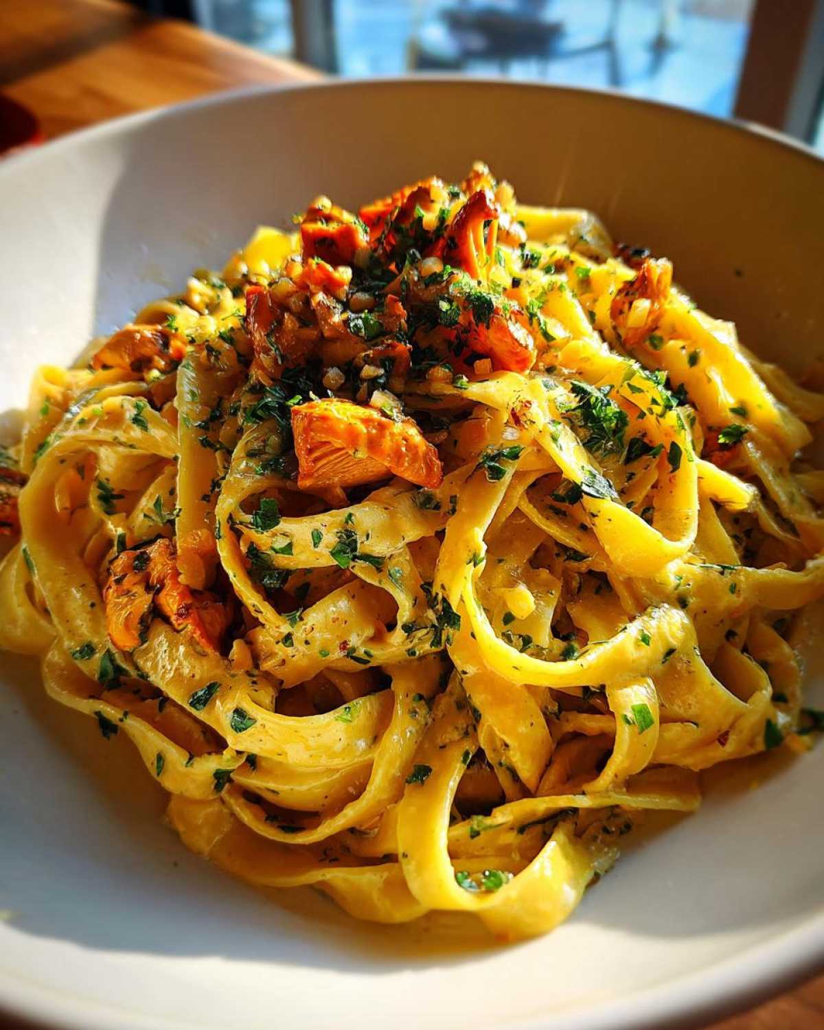 Zbliżenie na makaron tagliatelle z kurkami w kremowym sosie śmietanowym i posiekaną natką pietruszki.