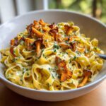 Zbliżenie na talerz pełen makaronu tagliatelle w kremowym sosie śmietanowym z kurkami i natką pietruszki – Makaron z kurkami w sosie śmietanowym.