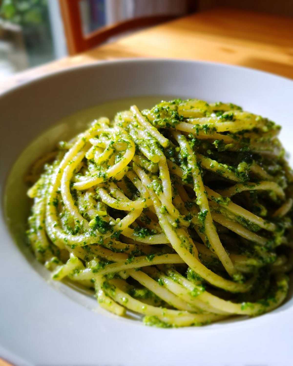 Porcja makaronu spaghetti obficie polana intensywnie zielonym Pesto z liści rzodkiewki w białej misce.