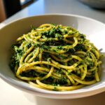 Zbliżenie na makaron spaghetti polany intensywnie zielonym Pesto z liści rzodkiewki w białej misce.