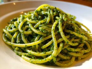 Zbliżenie na talerz makaronu spaghetti obficie polanego intensywnie zielonym Pesto z liści rzodkiewki.