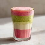 Warstwowe Matcha latte z musem truskawkowym w szklance, ukazujące różowe i zielone warstwy musu.
