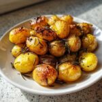 Złociste, pieczone młode ziemniaczki z rozmarynem i czosnkiem na białym talerzu.