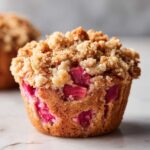 Zbliżenie na jedną muffinkę z rabarbarem i kruszonką, widoczne kawałki różowego rabarbaru i chrupiąca posypka.