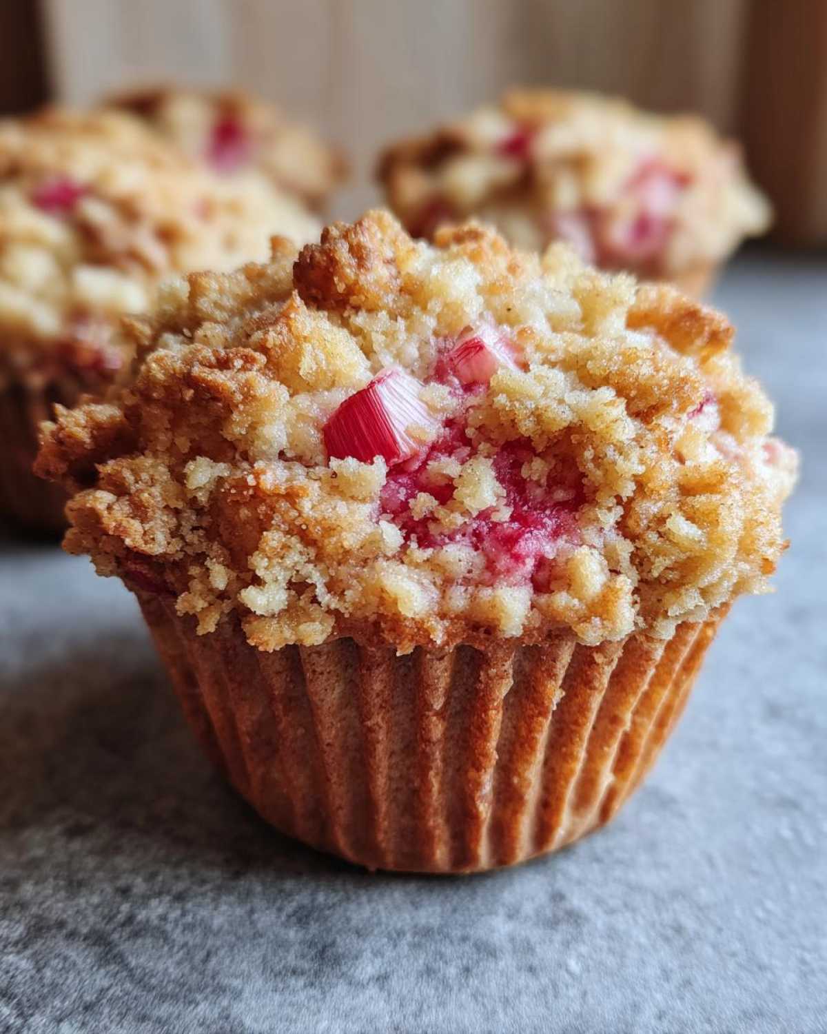 Zbliżenie na jedną z muffinek z rabarbarem i kruszonką, widoczna chrupiąca posypka i kawałki czerwonego rabarbaru.