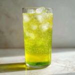 Szklanka musującego, jasnozielonego napoju funkcjonalnego z pędów sosny i cytryny z kostkami lodu.