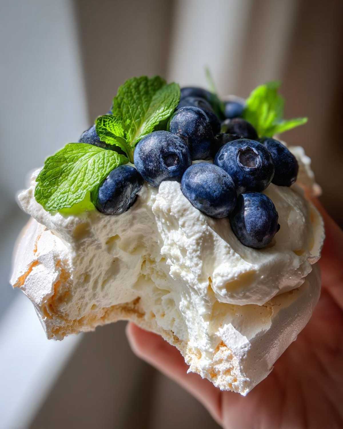 Zbliżenie na kawałek Pavlova z jagodami i miętą, ukazujące chrupiącą bezę i bitą śmietanę.
