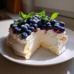 Przekrój Pavlova z jagodami i miętą, ukazujący chrupiącą bezę, krem i świeże owoce.