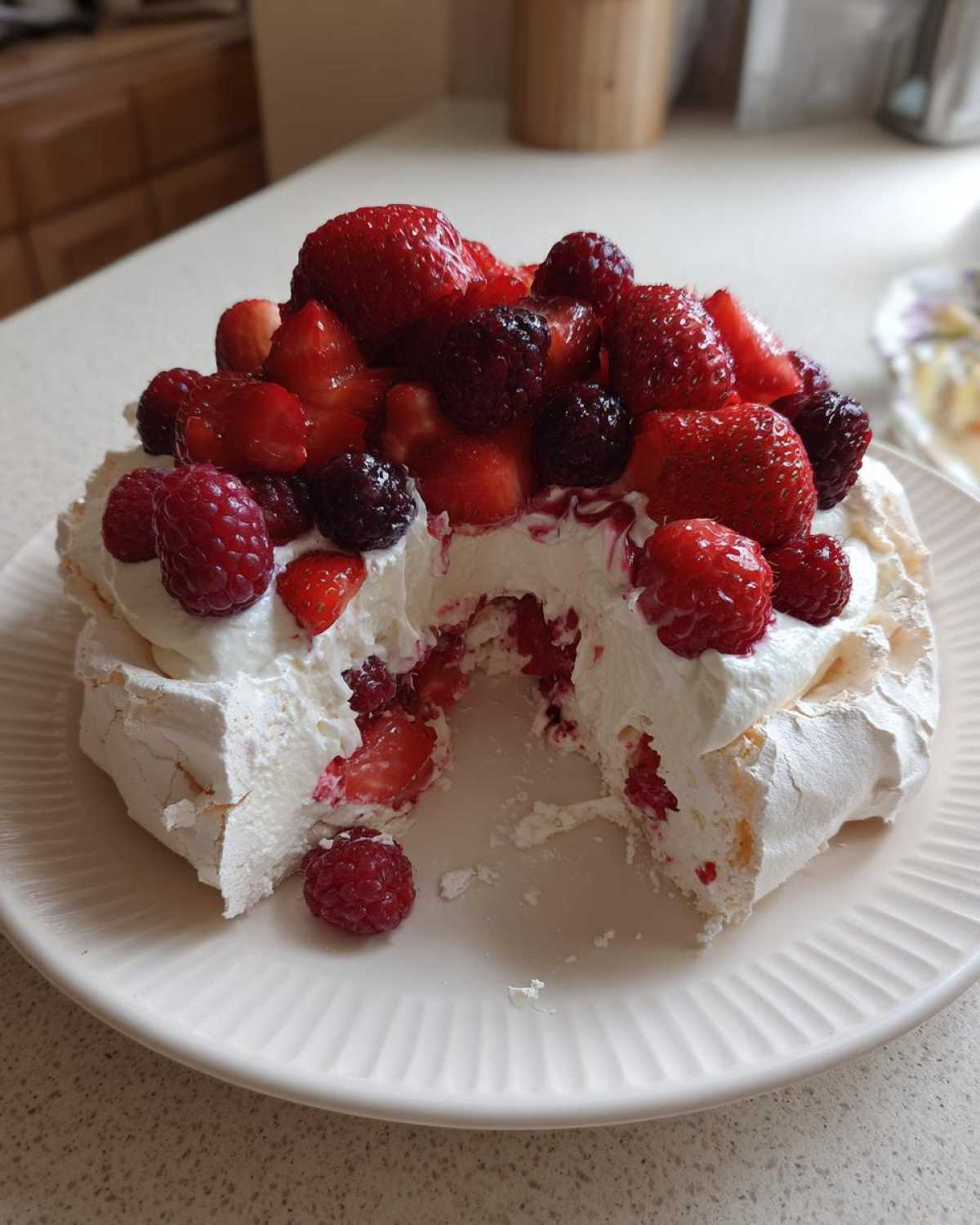 Zbliżenie na ukrojoną Pavlova z owocami jagodowymi, widoczne chrupiące bezy i krem.