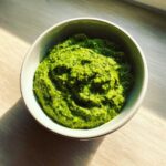 Intensywnie zielone Pesto z bobu z miętą i cytryną w jasnej miseczce na drewnianym blacie.