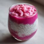 Warstwowy pudding chia z musem z rabarbaru w szklance, z widocznymi nasionami chia i intensywnie różową masą.