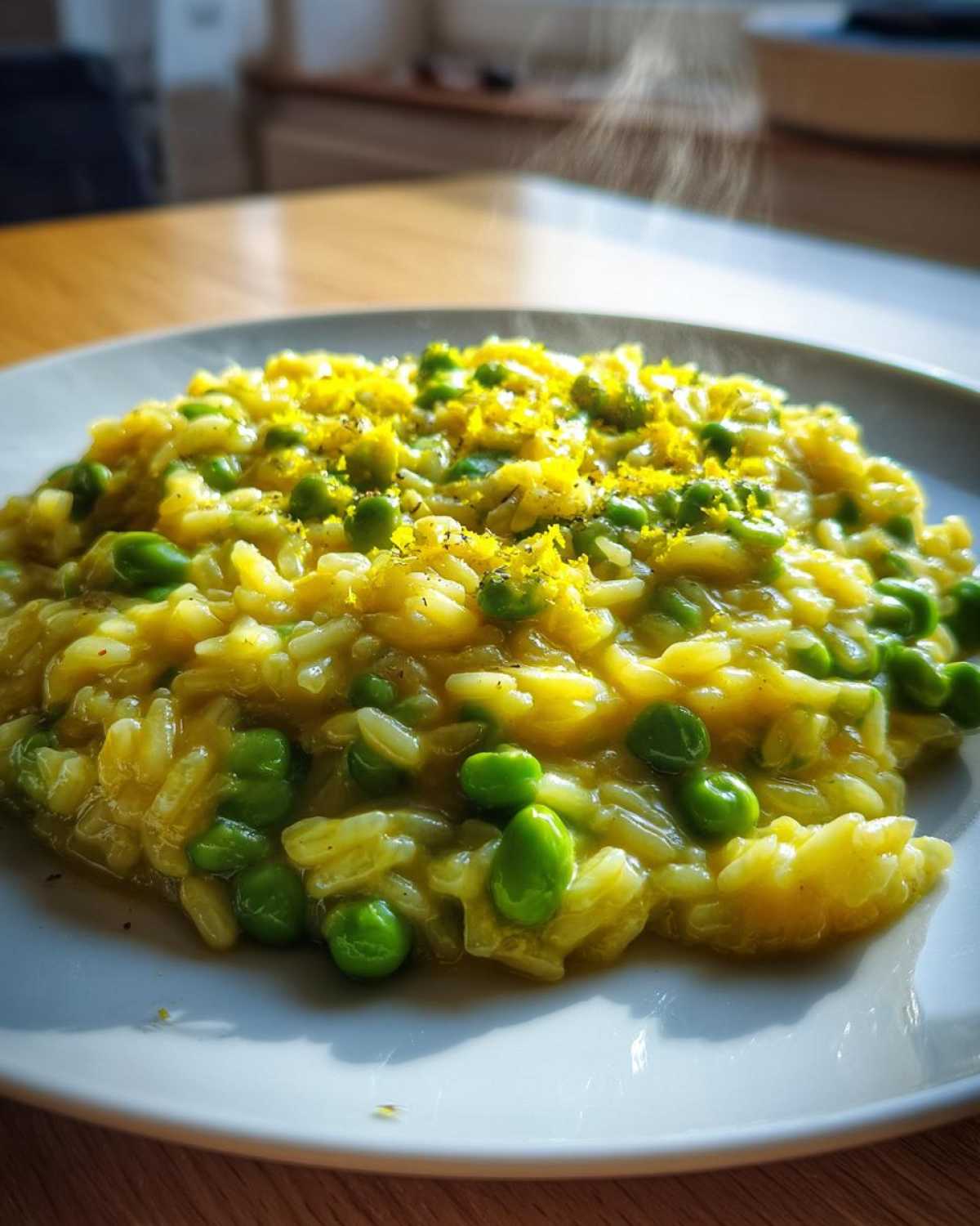 Kremowe Risotto z bobem i cytryną posypane skórką z cytryny, lekko parujące na białym talerzu.
