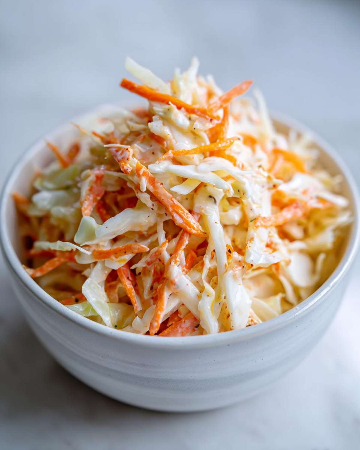 Zbliżenie na dużą porcję kremowej sałatki coleslaw z młodej kapusty i marchewki w białej misce.