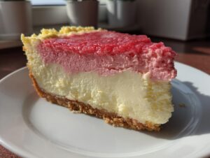 Kawałek sernika z białej czekolady z dwoma warstwami musu rabarbarowego na białym talerzu.