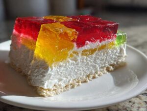 Kawałek sernik na zimno z kolorową galaretką, widoczna warstwa sera i kolorowe kostki galaretki.
