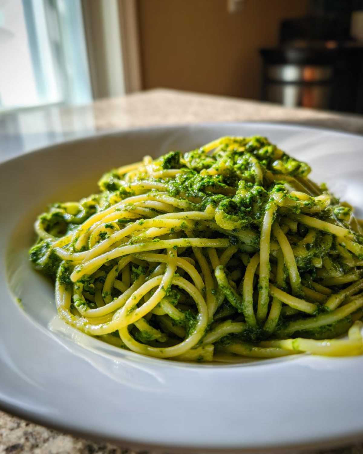 Zbliżenie na spaghetti polane intensywnie zielonym Pesto z liści rzodkiewki, podane na białym talerzu.