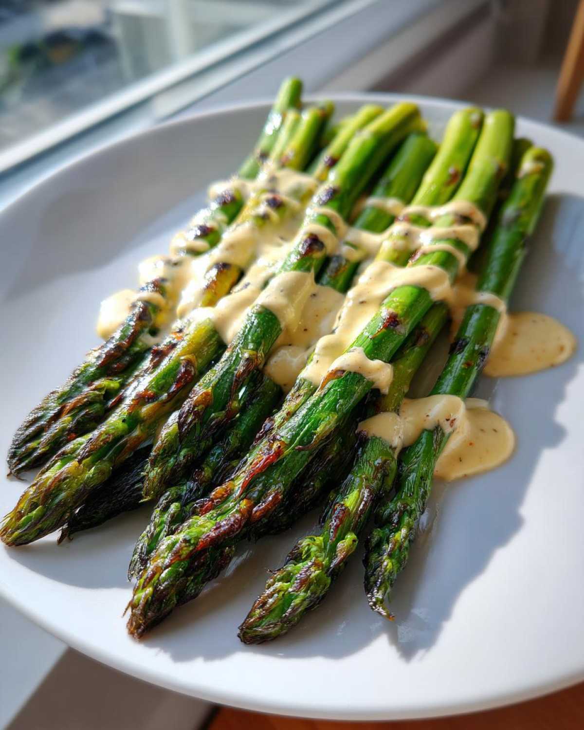 Pęczek grillowanych szparagów polanych kremowym sosem tahini, podany na białym talerzu.