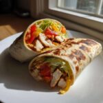 Przekrojona na pół tortilla z grillowanym kurczakiem i warzywami, ułożona na białym talerzu.