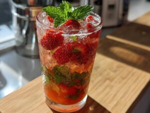 Szklanka pełna Truskawkowe Mojito bezalkoholowe z kawałkami truskawek, miętą i lodem.