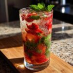 Zbliżenie na szklankę z Truskawkowym Mojito bezalkoholowym, pełne truskawek, mięty i lodu.